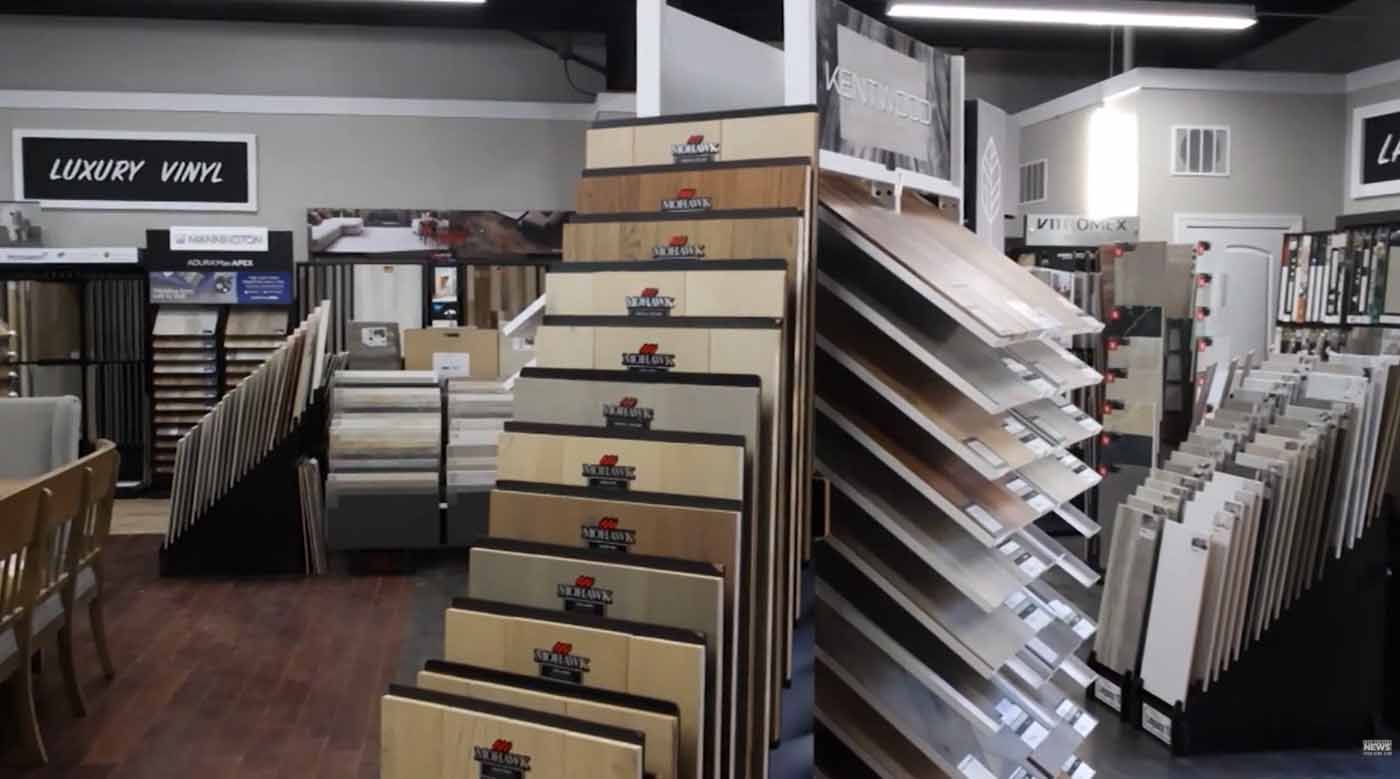 A carpet store aisle with racks of rugs and samples, including a tall rotating display in the foreground.