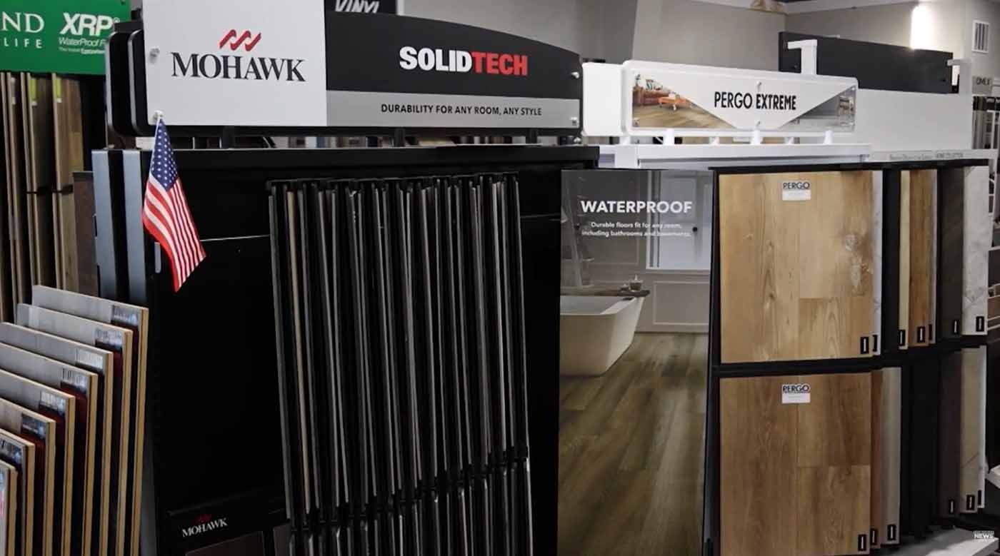 Flooring showroom display with sample racks, wood planks, and brand signs, including Mohawk and Waterpor™.