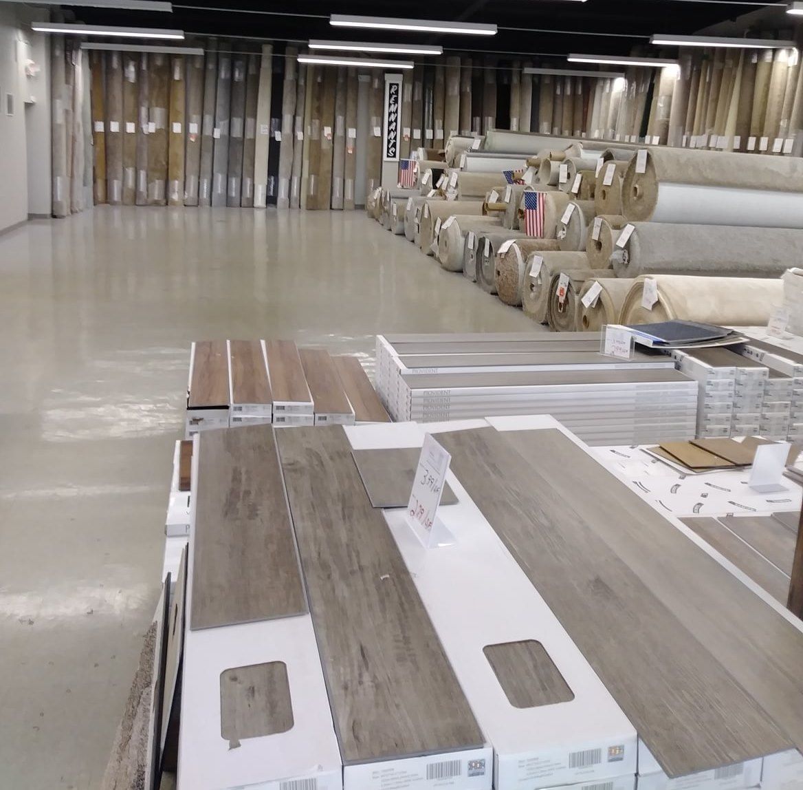 Flooring showroom with sample planks and rolled materials displayed on tables and racks