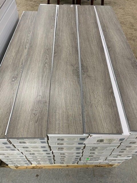 Stacked gray wood-look flooring planks on a pallet in a warehouse.