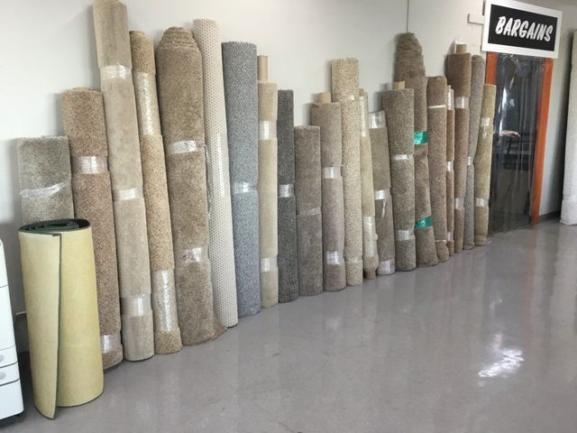 Rolled carpet samples stacked along a wall in a showroom, with a door labeled “AGARAN” nearby