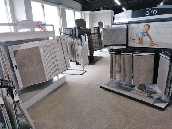 Carpet showroom with display racks of patterned rugs and samples under bright overhead lights