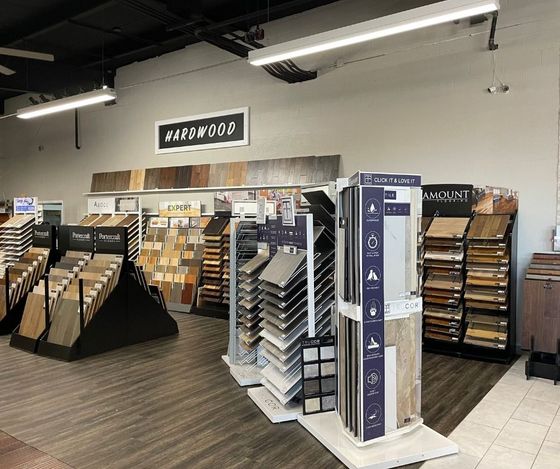 Flooring store aisle with carpet and tile displays, sample racks, and a “Warehouse” sign.
