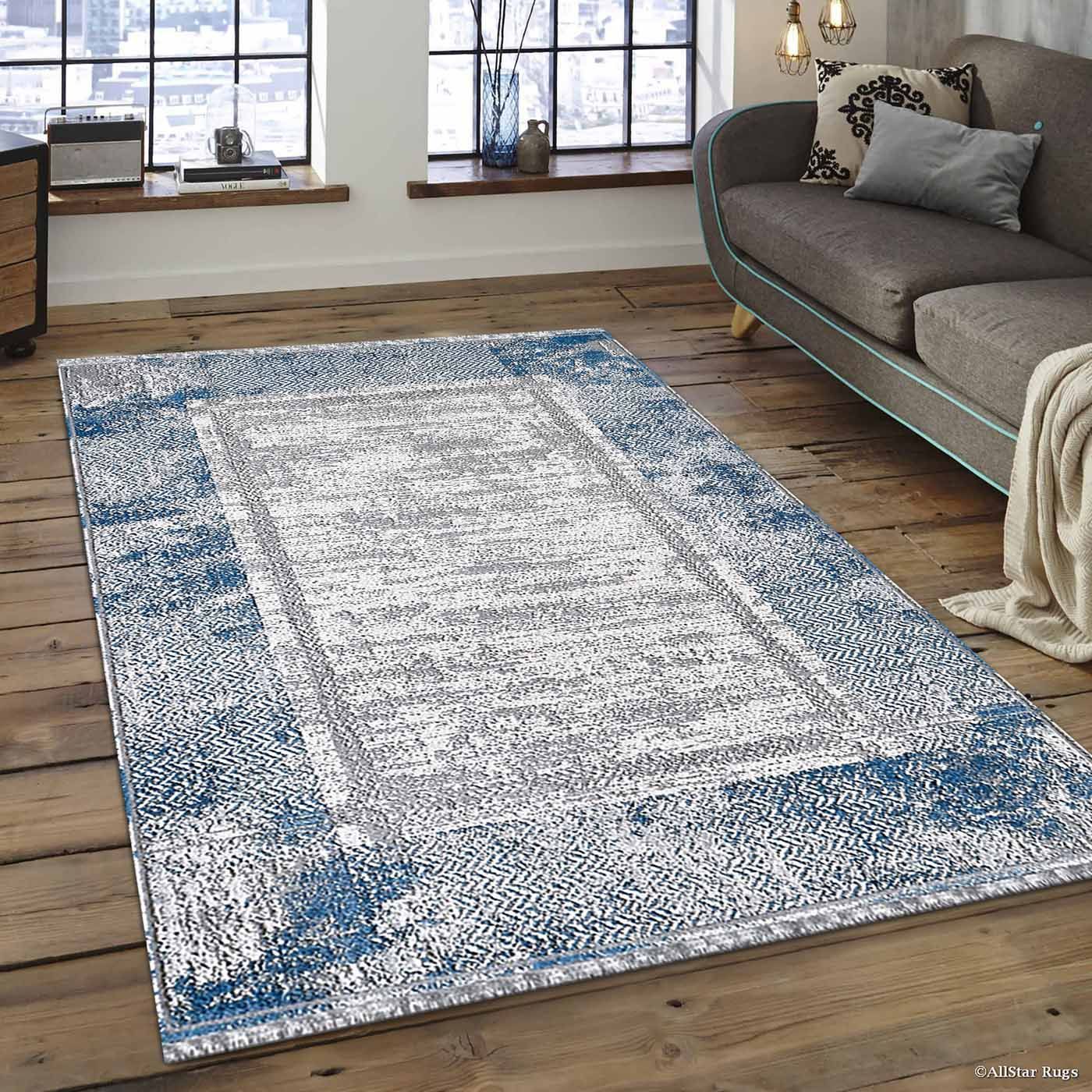 Blue-and-white area rug on a wooden floor beside a gray sofa in a sunlit living room.