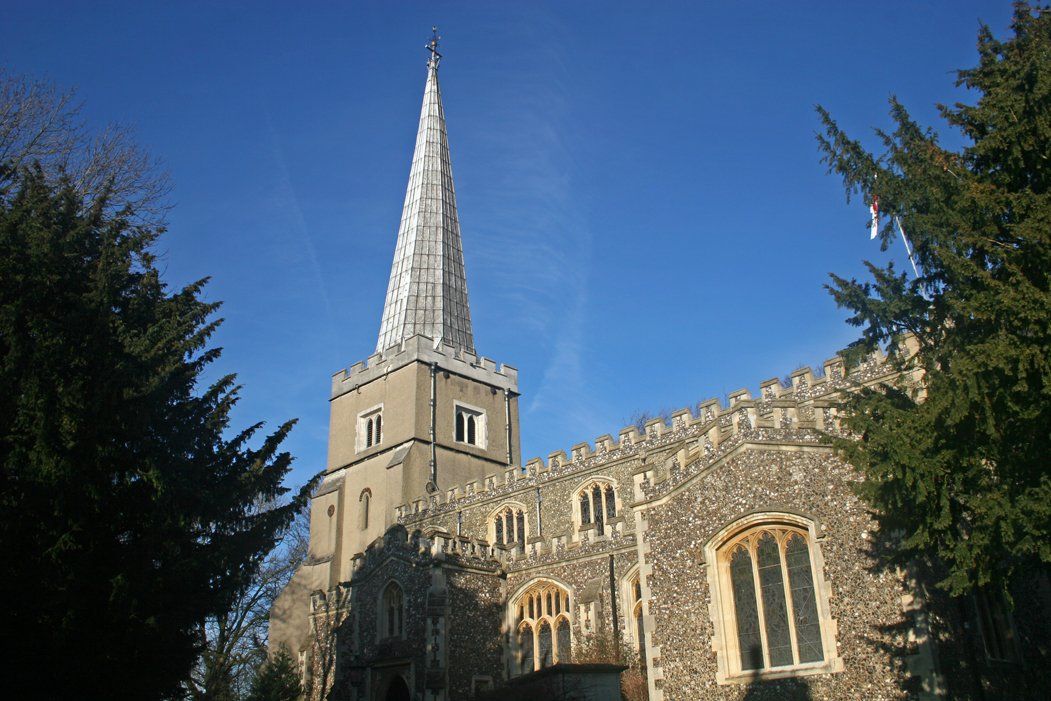 Stone church with tall spire against a clear blue sky, framed by trees