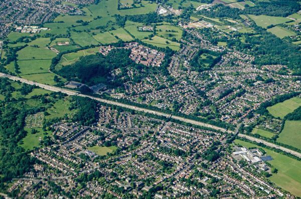 Aerial view of a town with a highway cutting through green fields and dense neighborhoods.