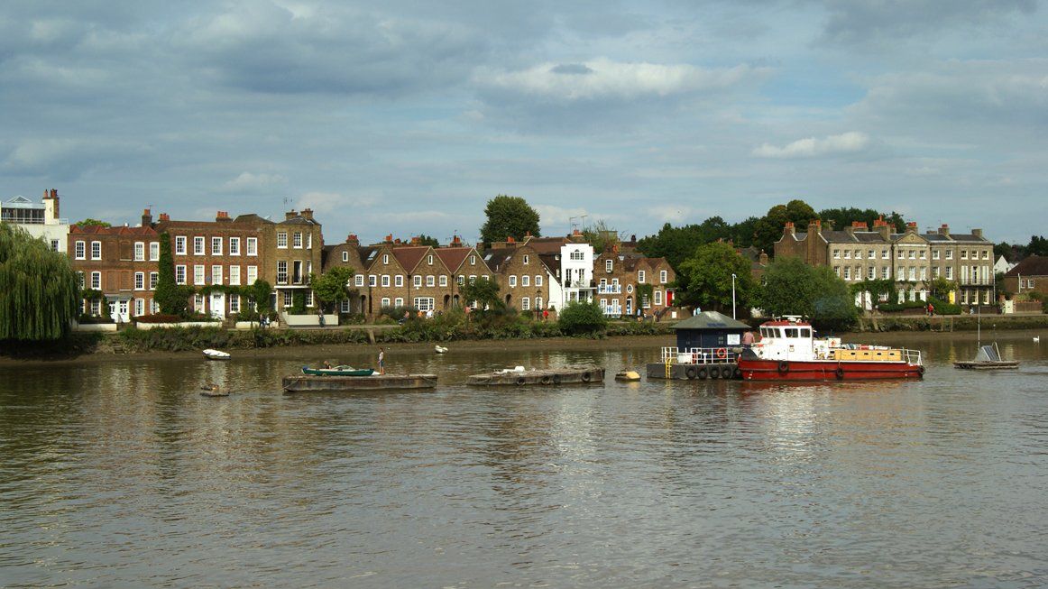 Riverside town skyline with brick houses and a small red-and-white boat on calm water