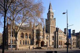 Historic stone civic building with a clock tower and arched windows on a city street