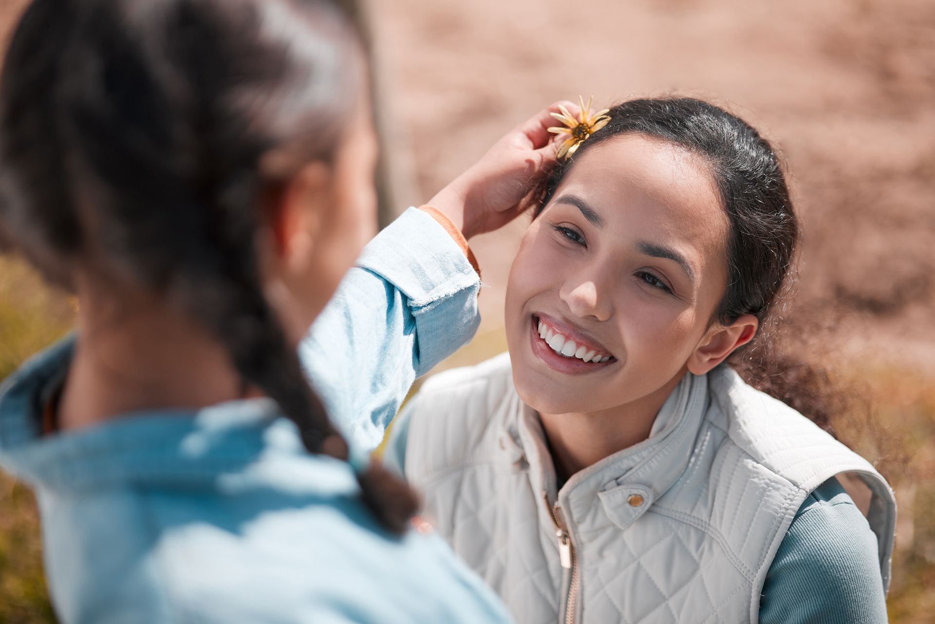A person placing a small flower in another person's hair while both smile outdoors.
