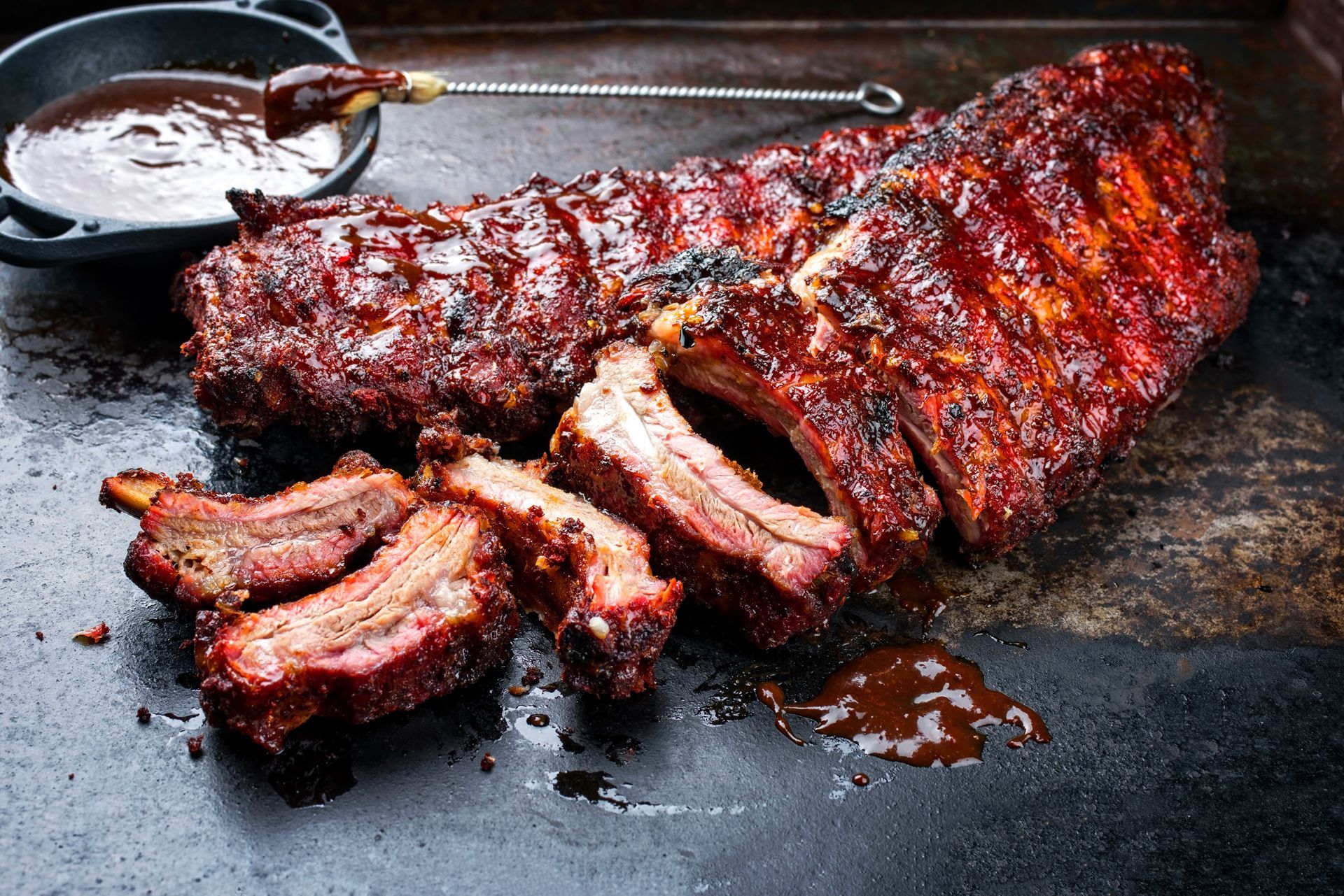 A large piece of meat is sitting on a table next to a bowl of sauce