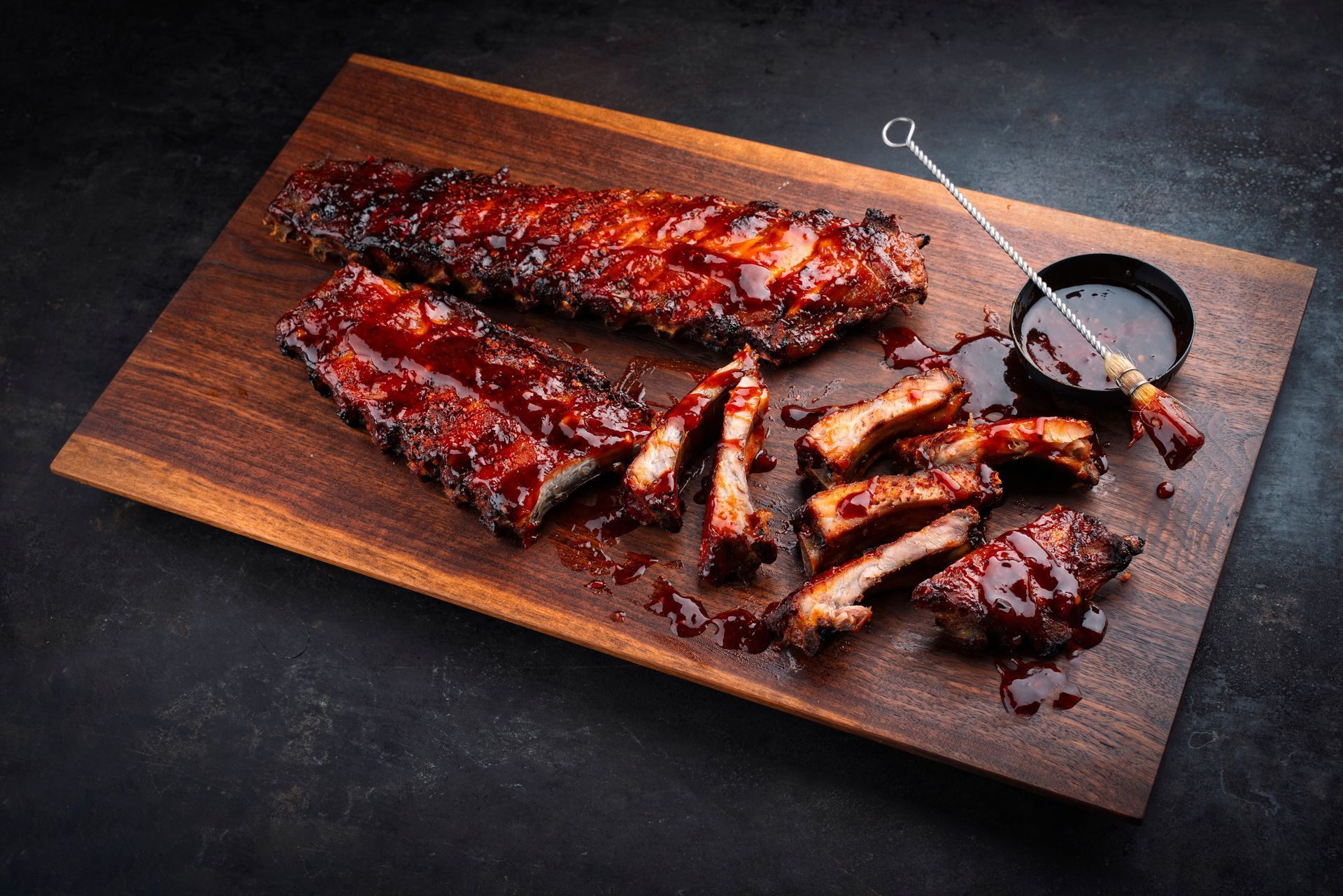 A wooden cutting board topped with ribs and sauce