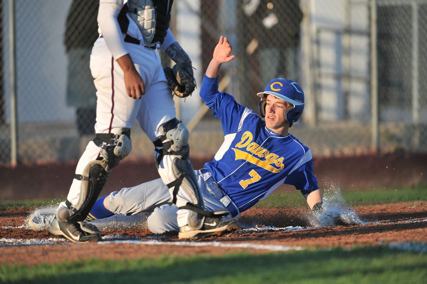 Baseball player sliding into home plate, catcher in front. Blue and gold uniforms, action shot.