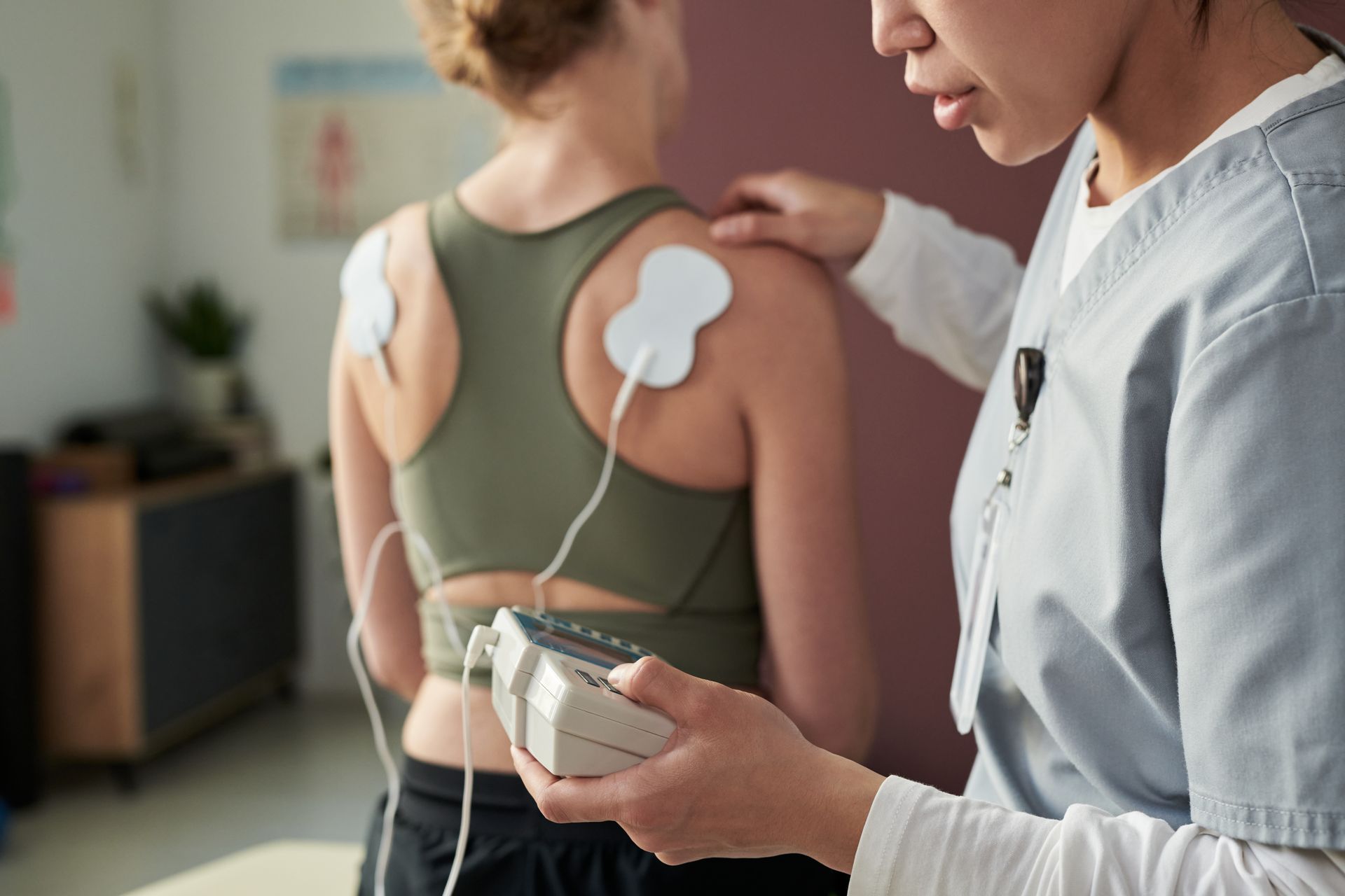 Physical therapist adjusting a muscle stim device on a patient’s back with electrodes attached
