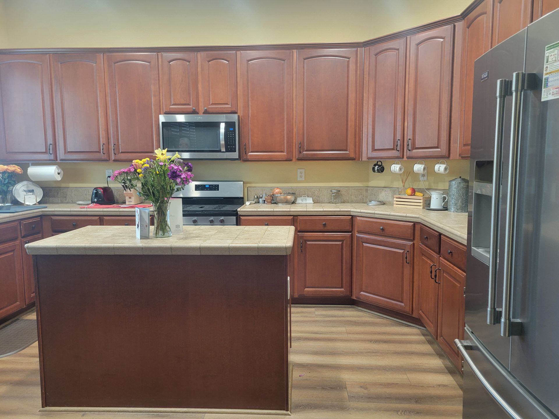 Modern kitchen with wooden cabinets, granite island, stainless steel appliances, and flowers on the counter