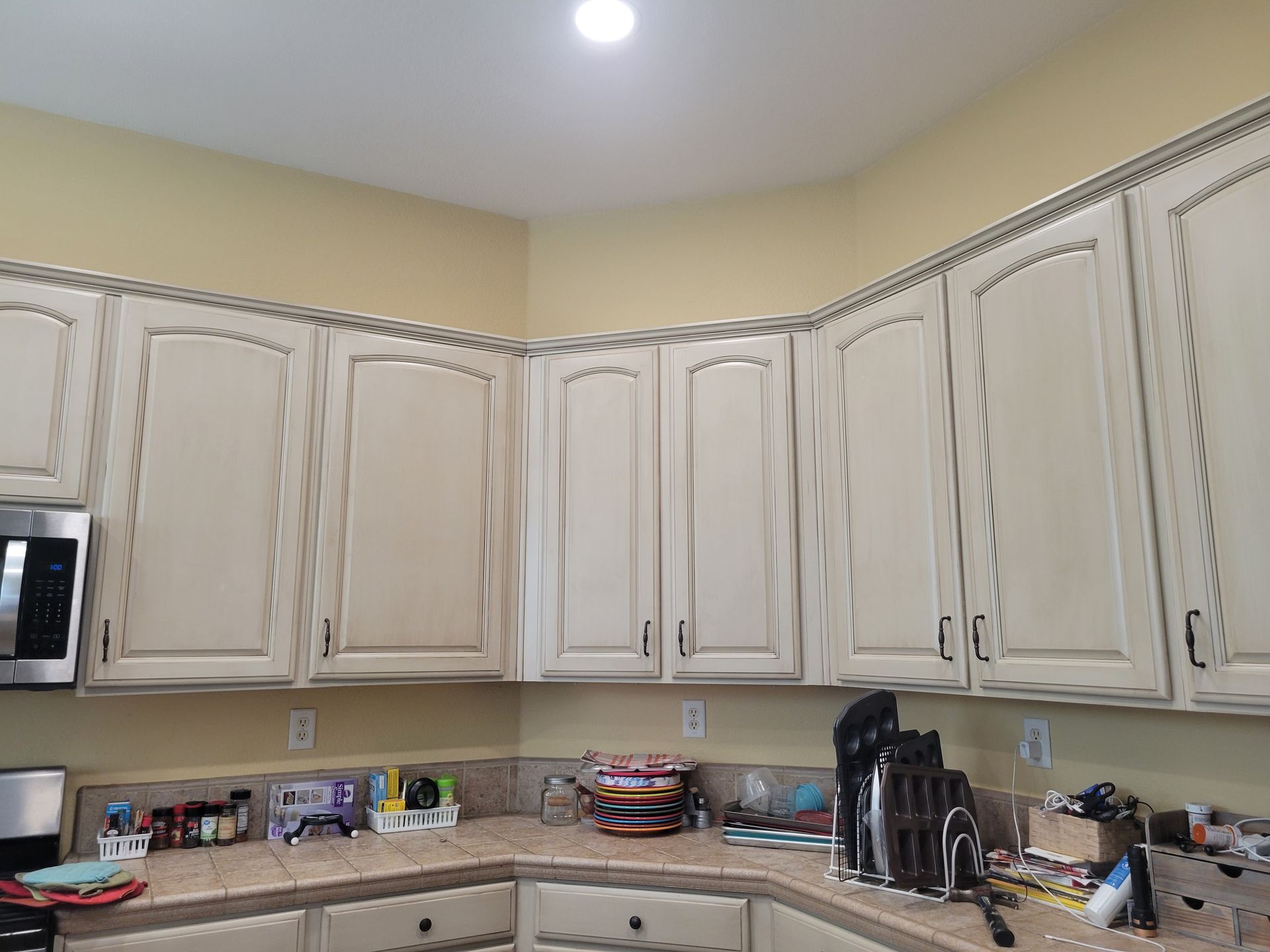 Kitchen with cream-colored cabinets, beige walls, and a countertop holding assorted items and appliances