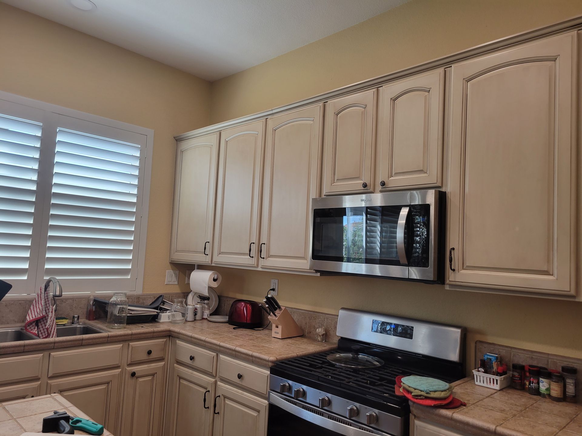 Kitchen with beige cabinets, stainless microwave, gas stove, and a window with white blinds.
