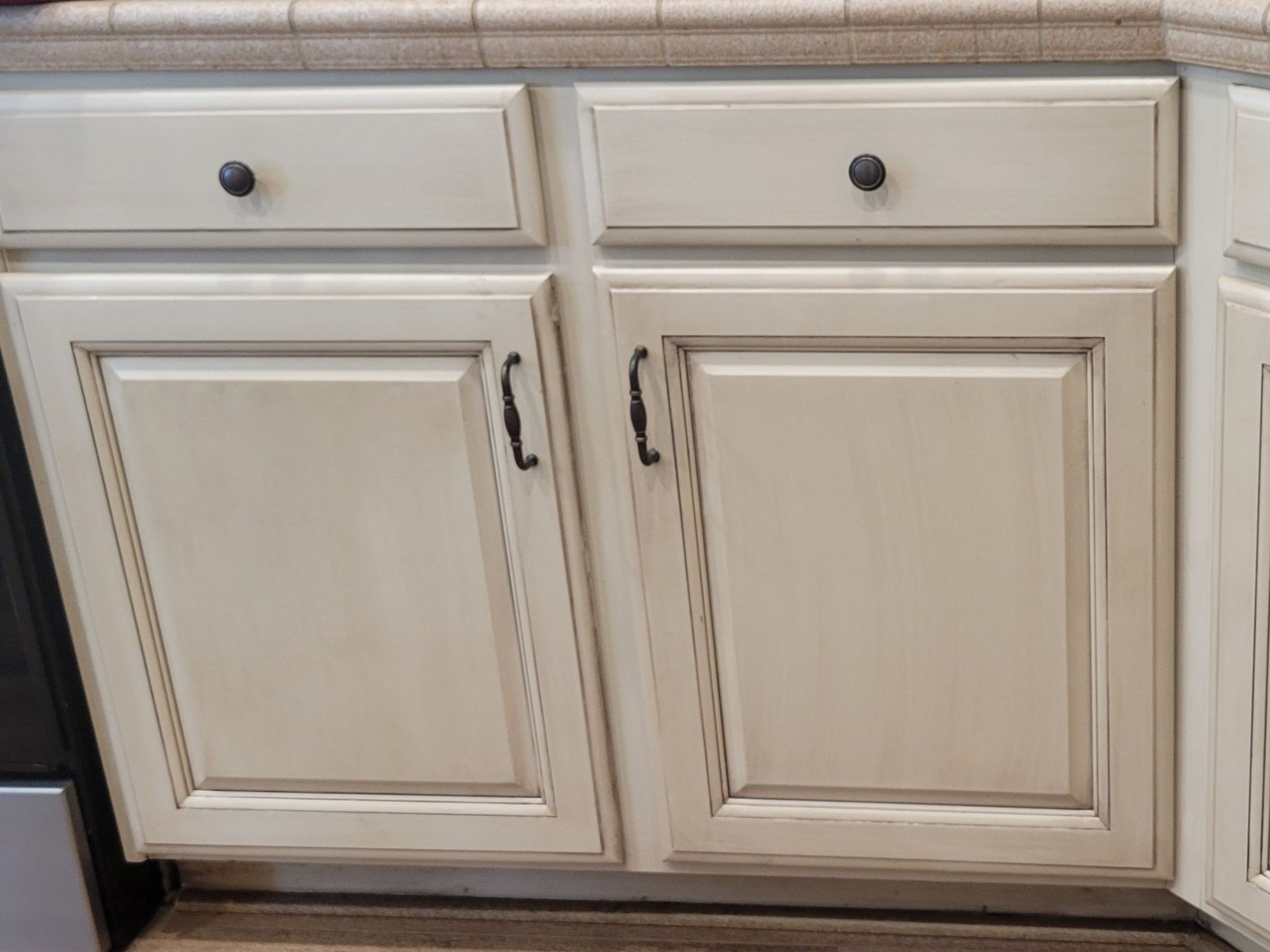 Cream kitchen cabinet with two drawers and two paneled doors with black knobs and handles
