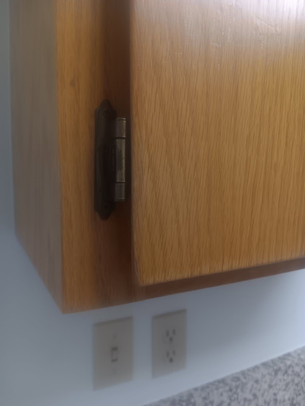 Close-up of a wooden cabinet corner with two wall outlets below it.