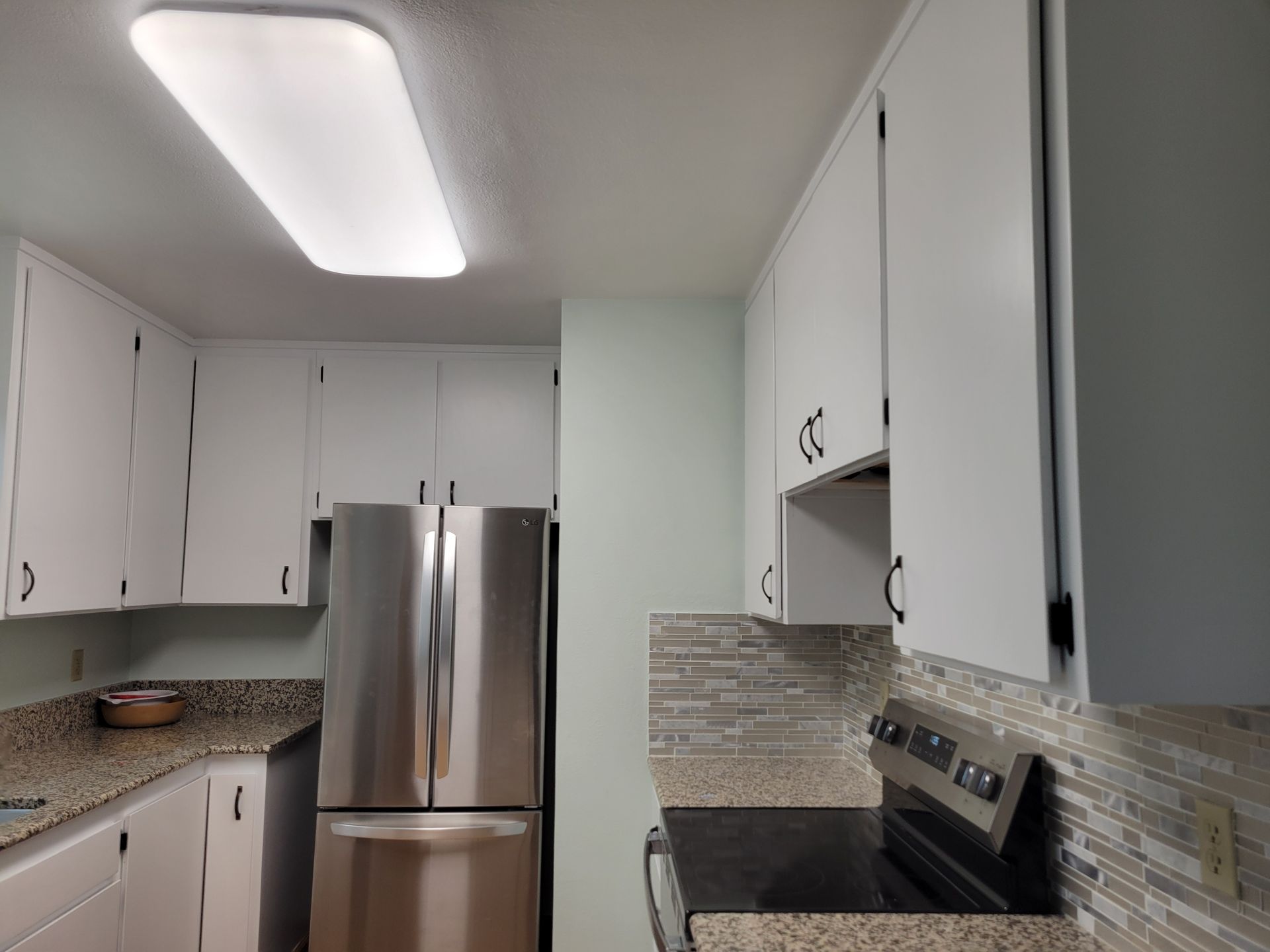 Bright modern kitchen with white cabinets, stainless steel fridge, and black stove under a skylight.