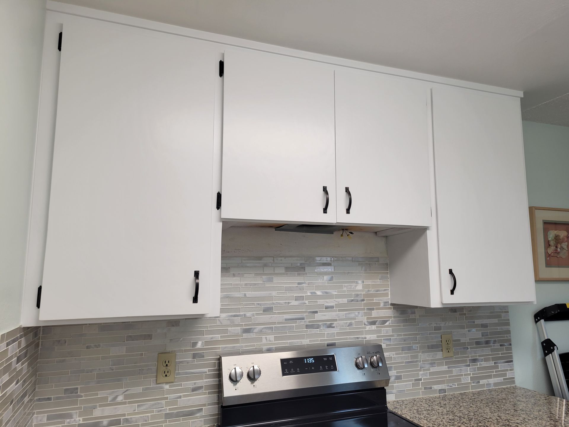 White kitchen cabinets above a stainless steel stove and gray tile backsplash