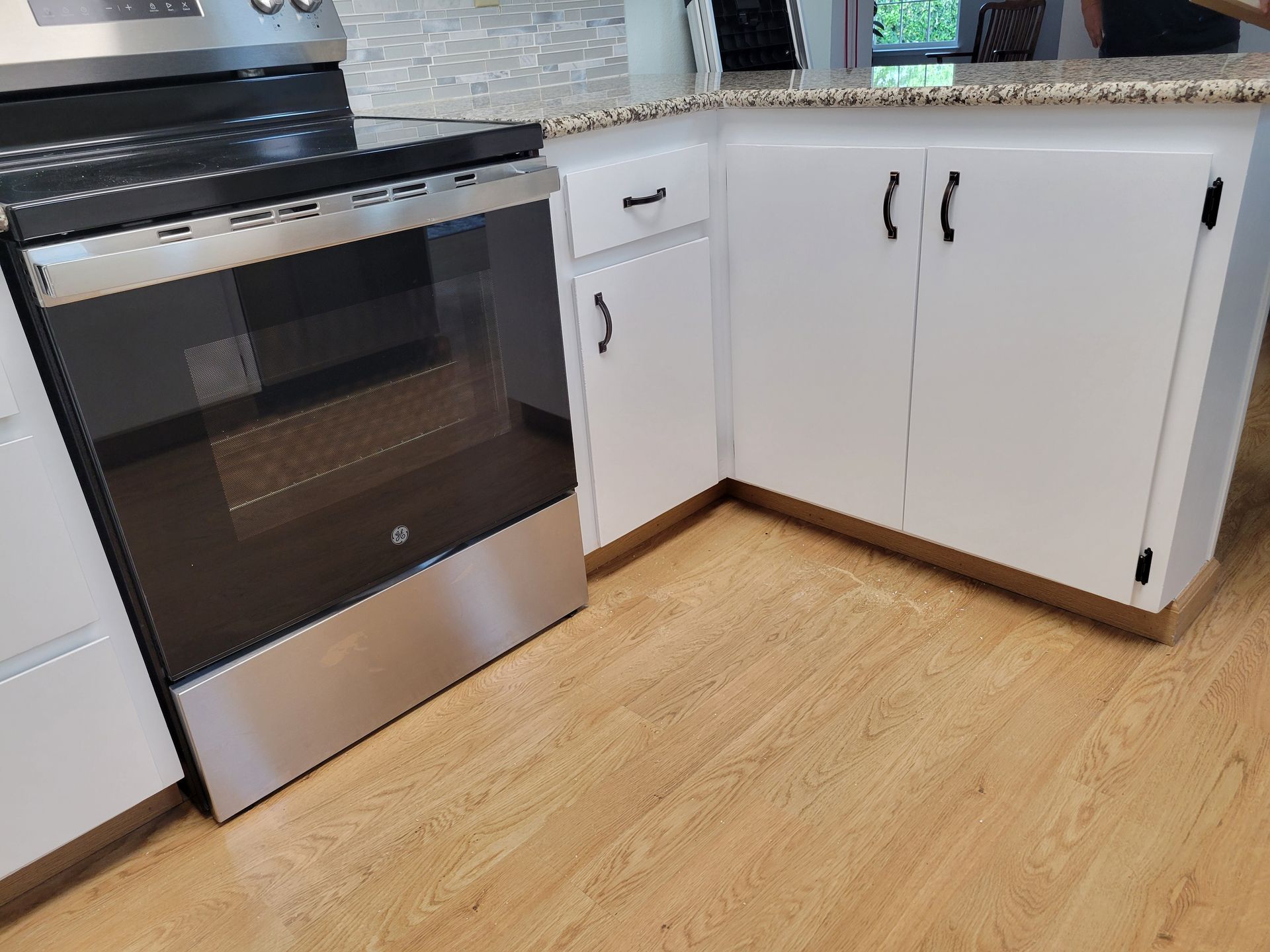Kitchen corner with stainless steel oven, white cabinets, granite countertop, and light wood floor