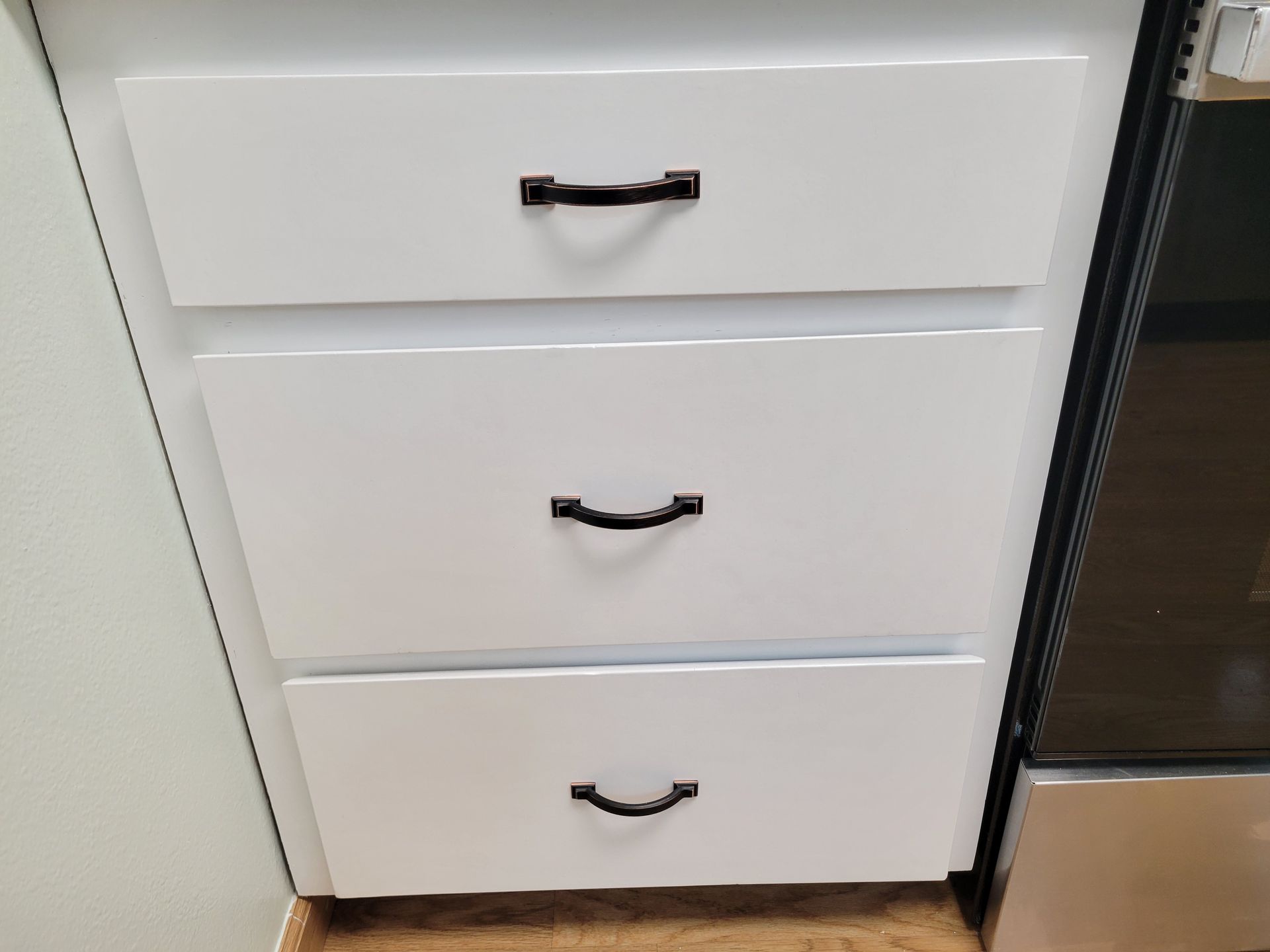 White cabinet drawers with black handles beside a stainless steel appliance.