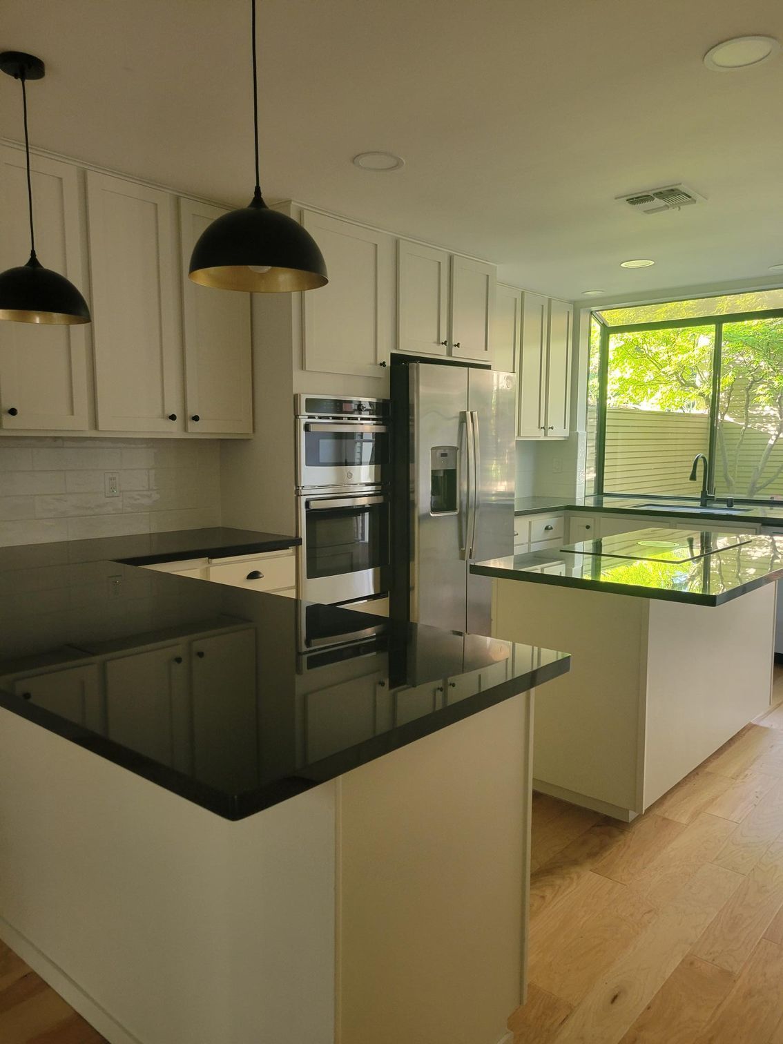 Modern kitchen with white cabinets, black countertops, stainless appliances, and a window overlooking greenery