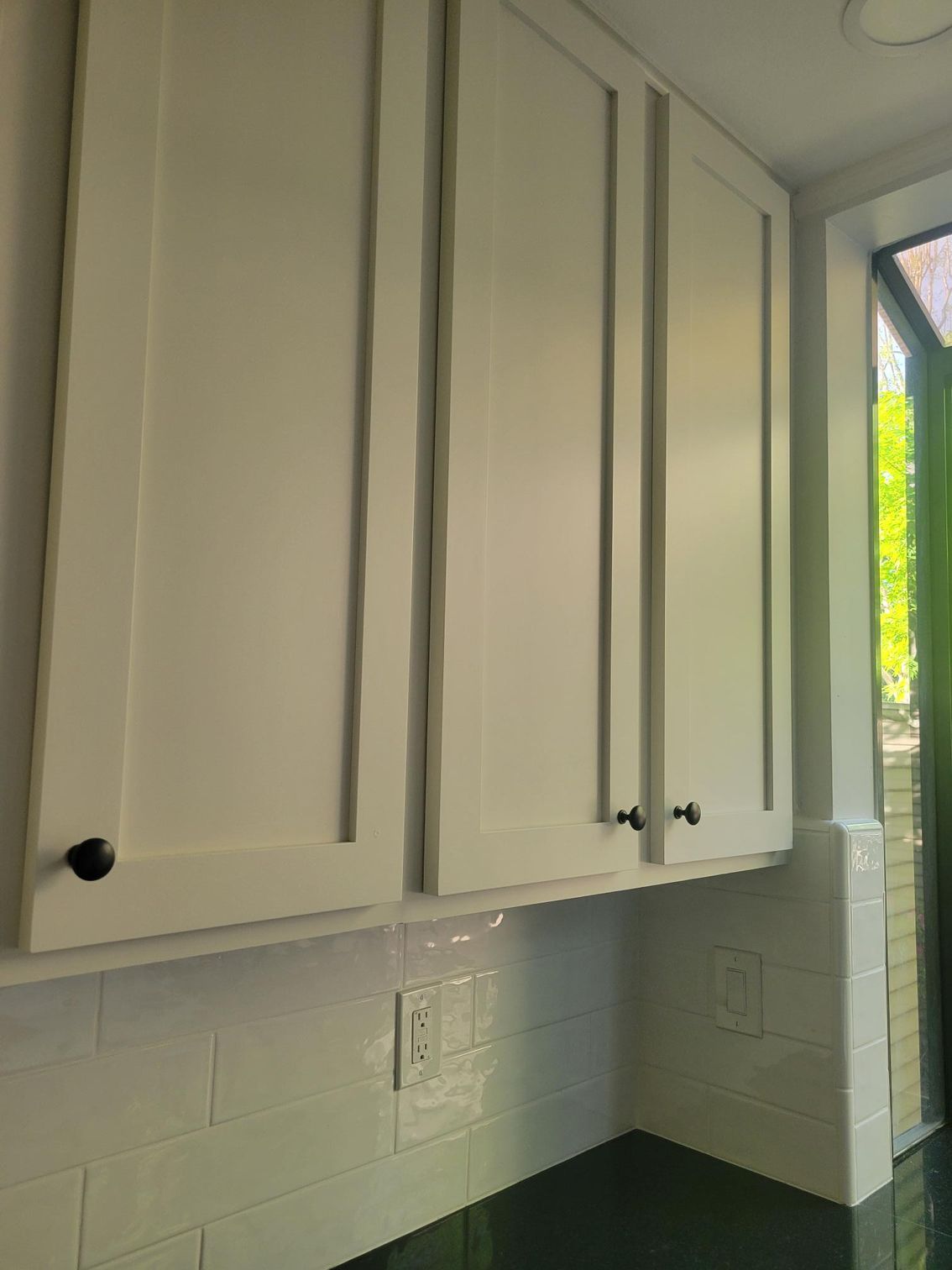 White kitchen cabinets above a tiled backsplash and countertop by a window