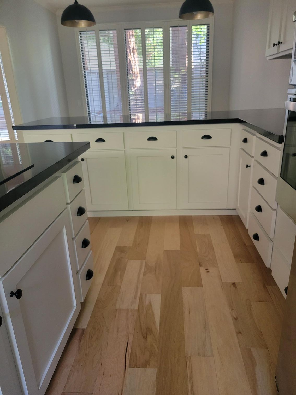 Bright kitchen with white cabinets, black countertops, wood floor, and window blinds.