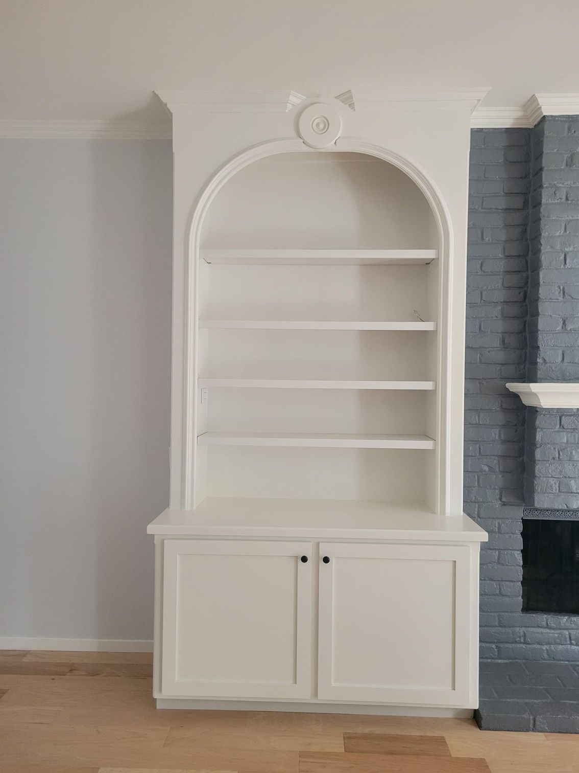 White built-in arched bookcase with cabinet doors in a room beside a gray brick fireplace.