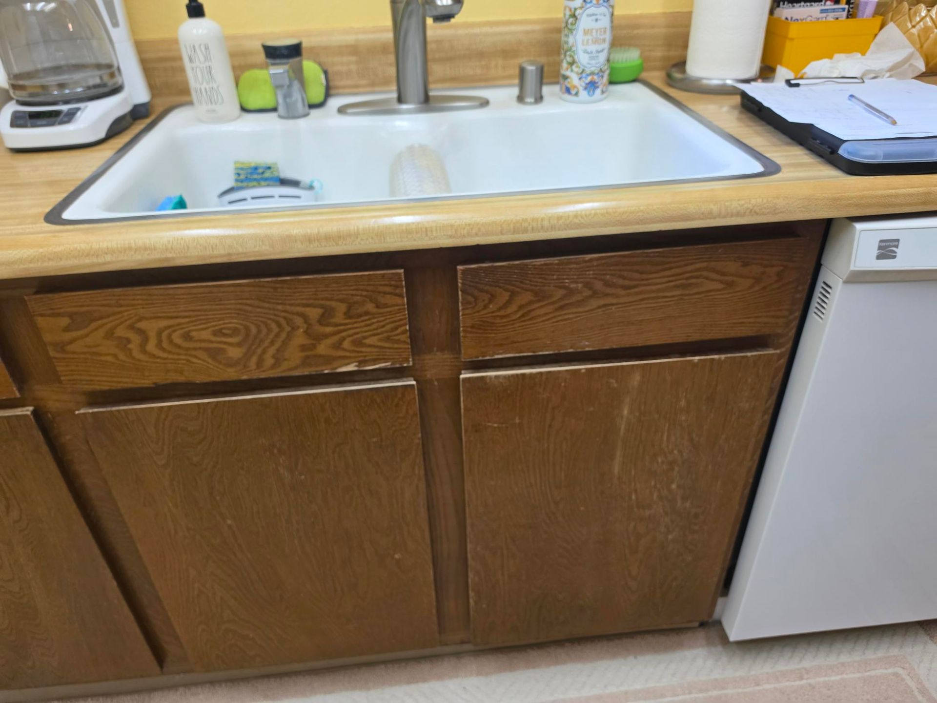 Kitchen sink and wooden cabinets with countertop items and a dishwasher on the right.