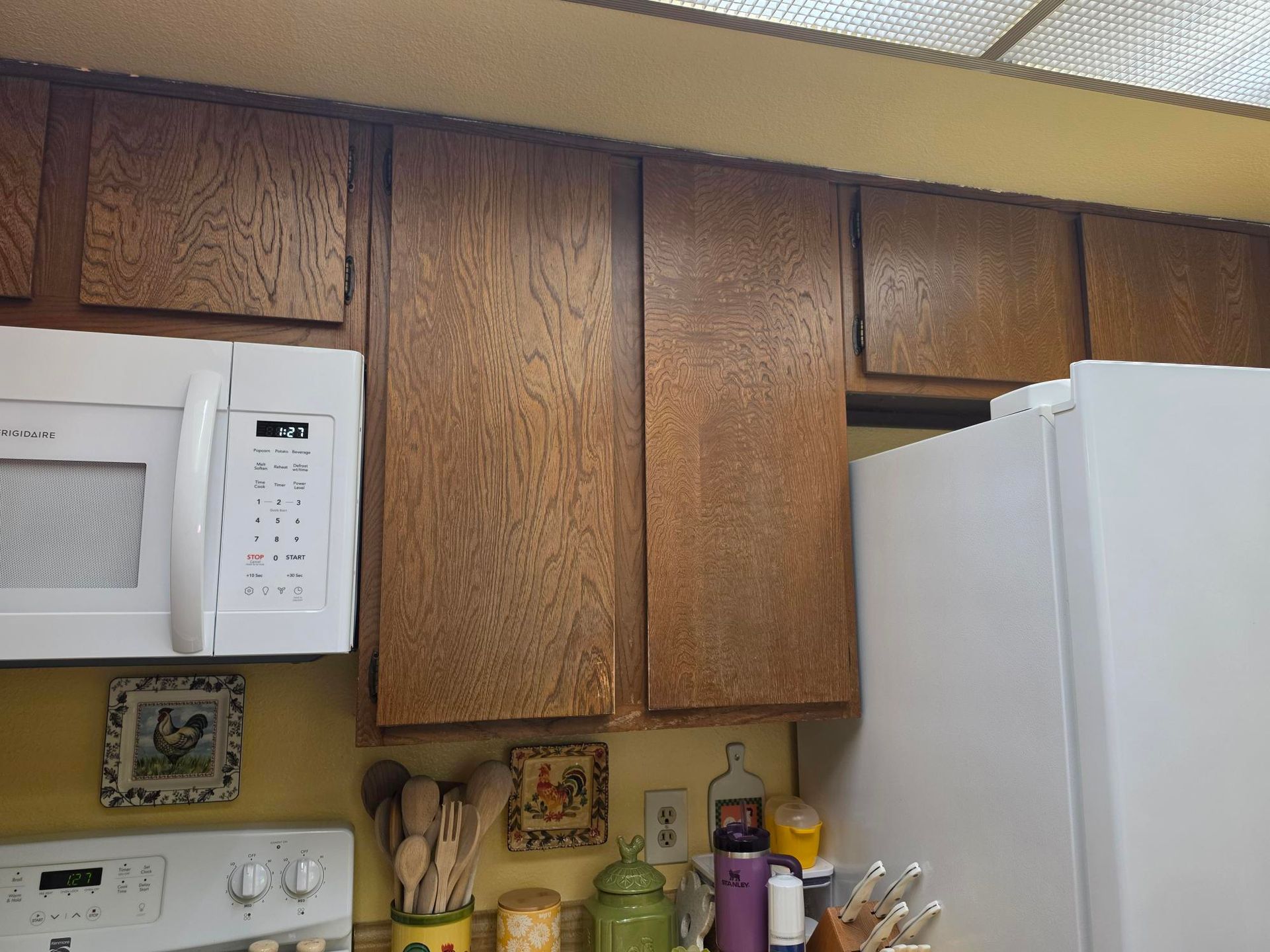 Kitchen with wooden cabinets, white microwave, and refrigerator under a drop ceiling.