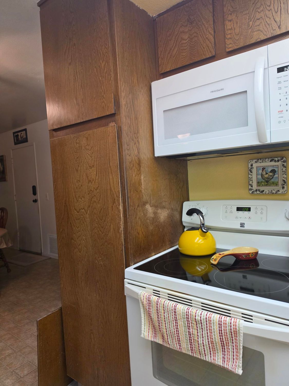 Kitchen with wood-paneled walls, white microwave above stove, yellow kettle, and striped towel on oven door.