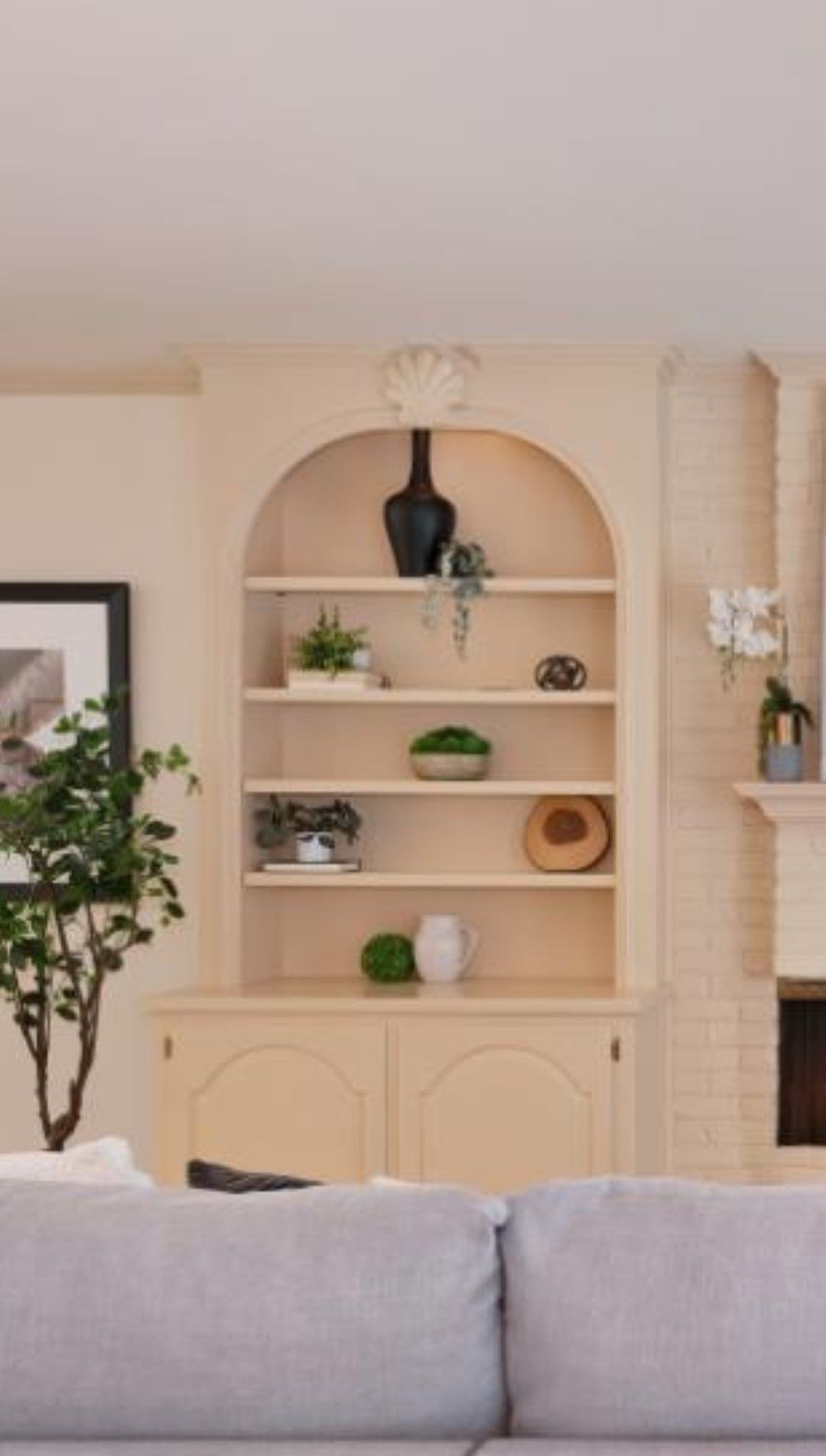 Built-in beige wall shelves with decor above a gray sofa in a bright living room