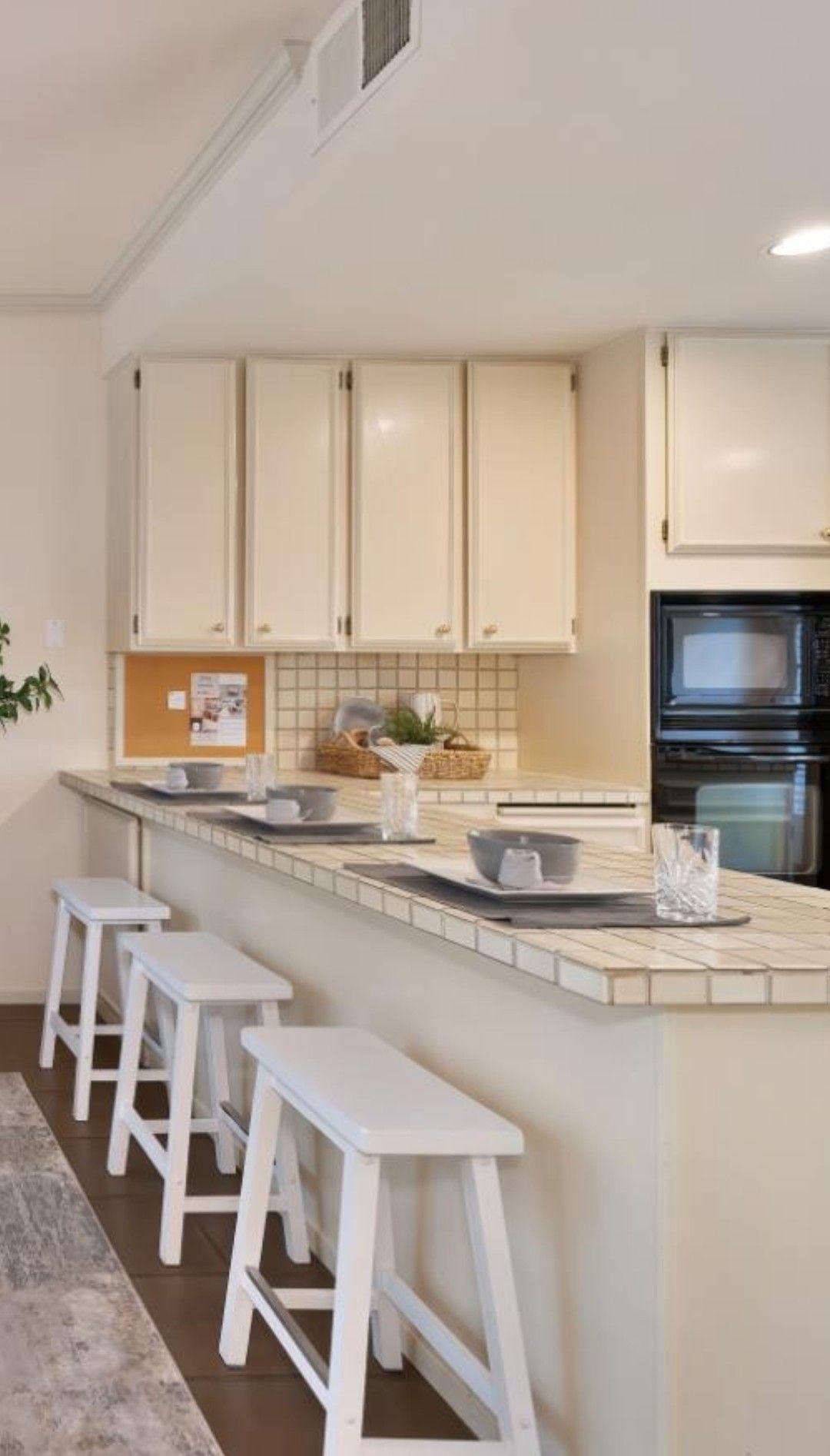 Bright white kitchen with bar stools, island, beige cabinets, and built-in oven under slanted ceiling