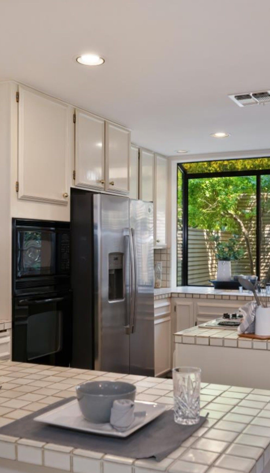 Modern kitchen with stainless steel fridge, white cabinets, and a tiled island by a bright window.