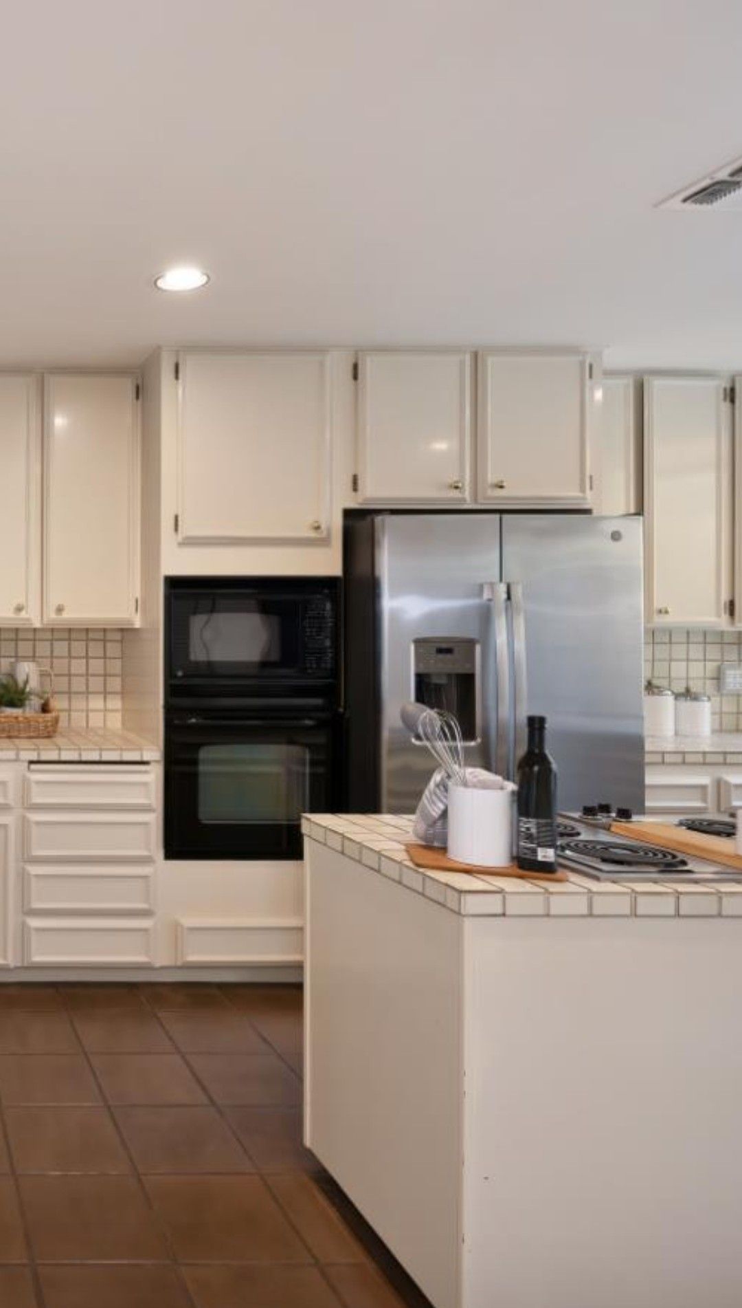 Modern kitchen with white cabinets, stainless steel fridge, and a central island on tile flooring