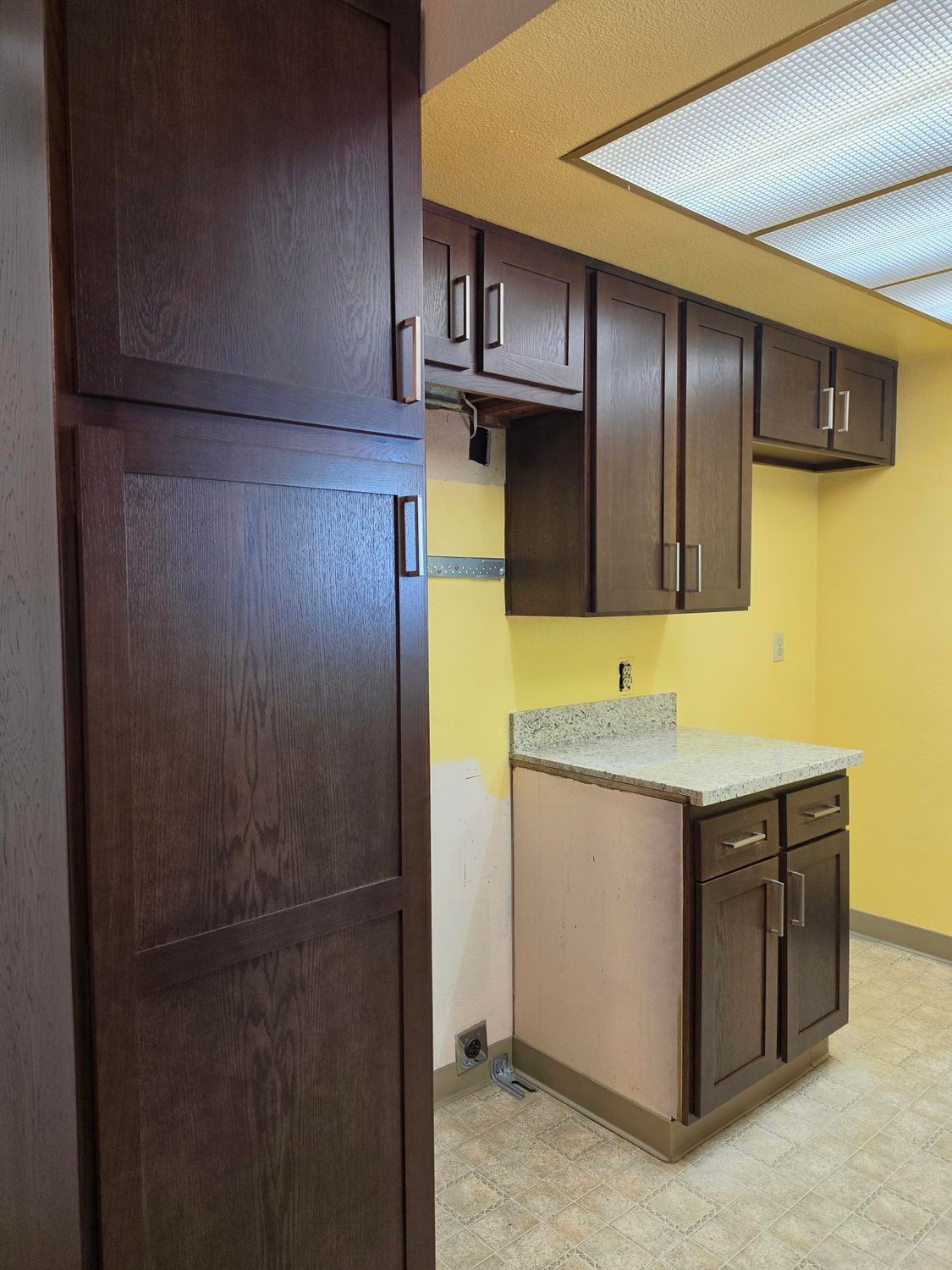 Empty kitchen with dark wood cabinets, yellow walls, and a speckled countertop sink area.