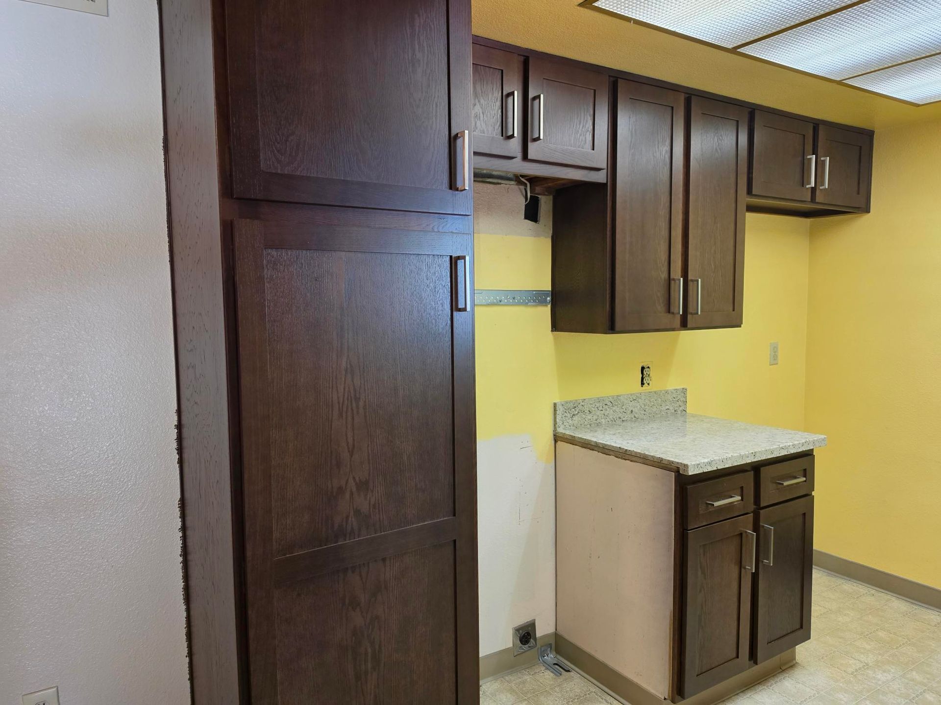 Small kitchen with dark wood cabinets, yellow wall, and a white countertop on a lower cabinet.