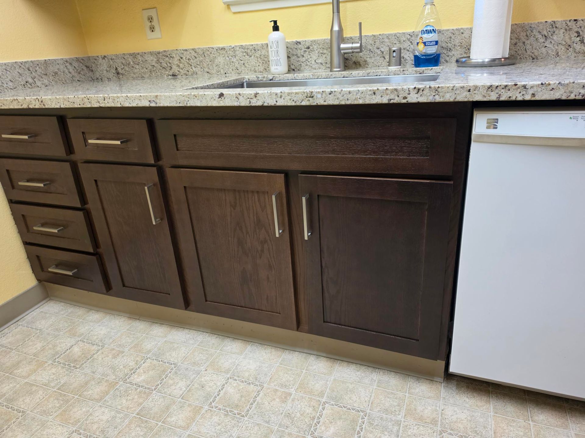 Kitchen counter with dark brown cabinets, beige speckled countertop, and a white dishwasher under the sink area