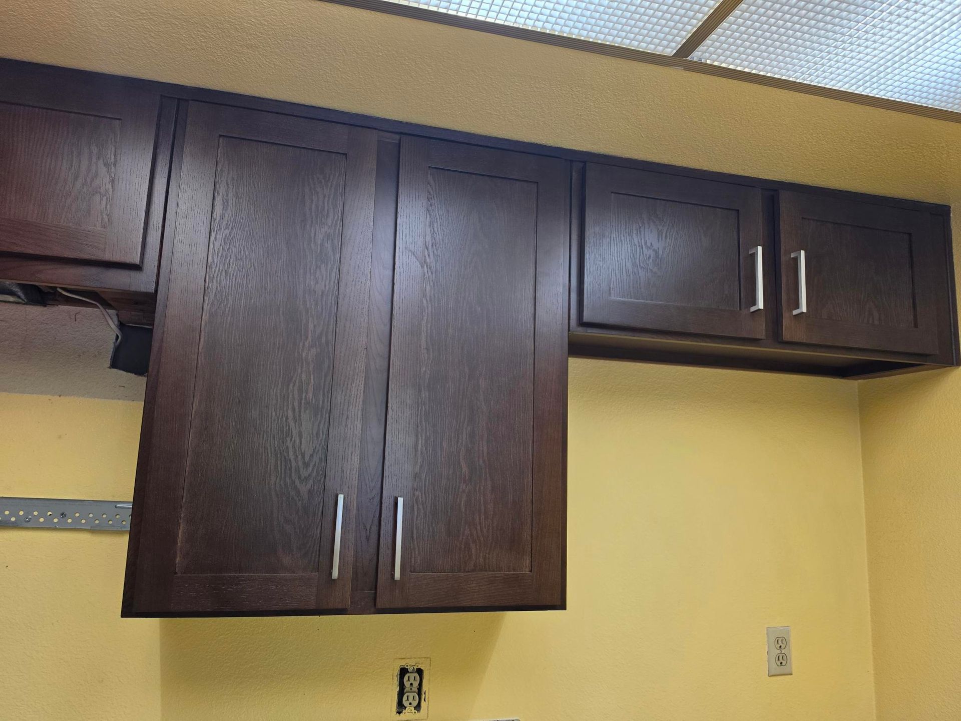 Dark wood kitchen wall cabinets mounted above a yellow wall with metal handles