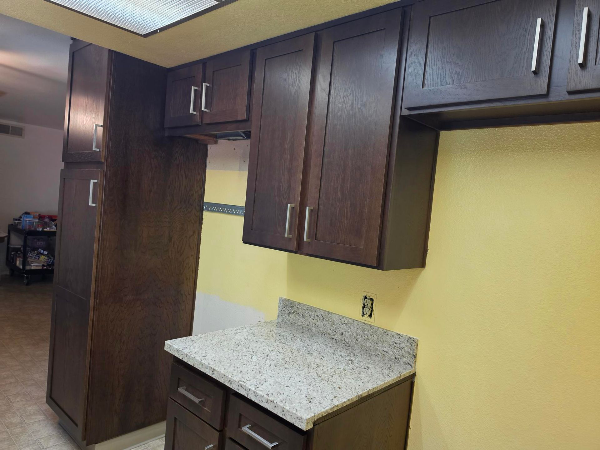 Empty kitchen corner with dark wood cabinets, speckled countertop, and yellow walls.
