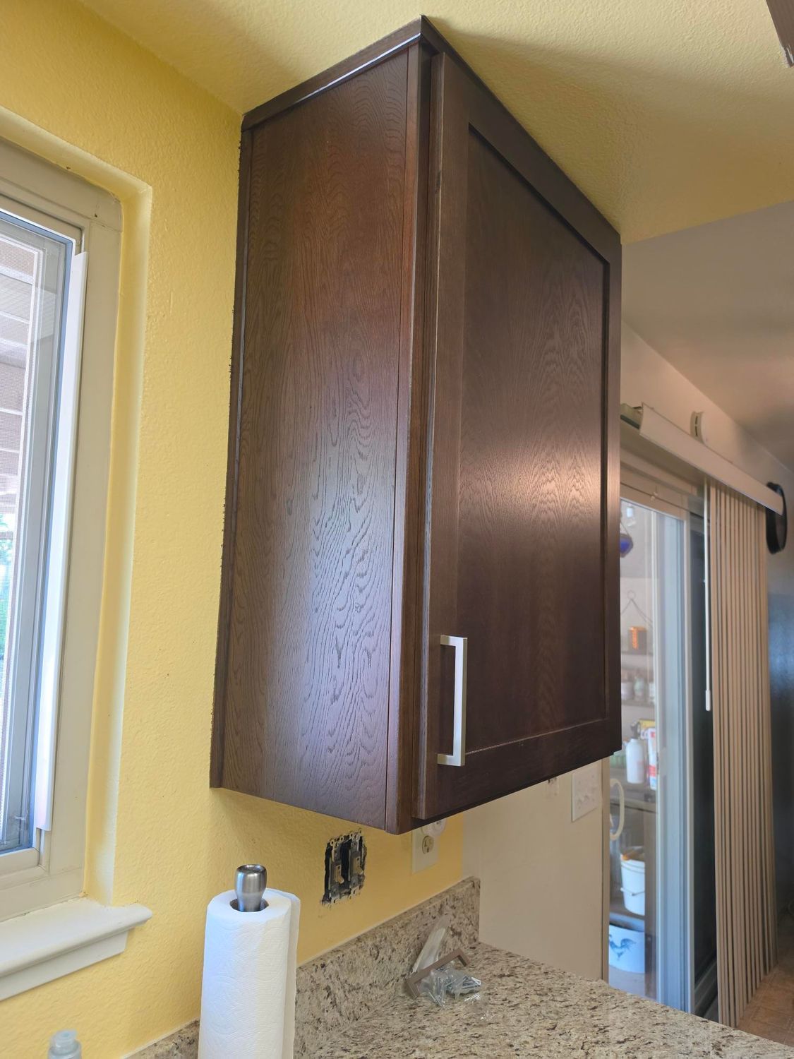 Dark wood kitchen cabinet above a granite countertop beside a window and sliding glass door