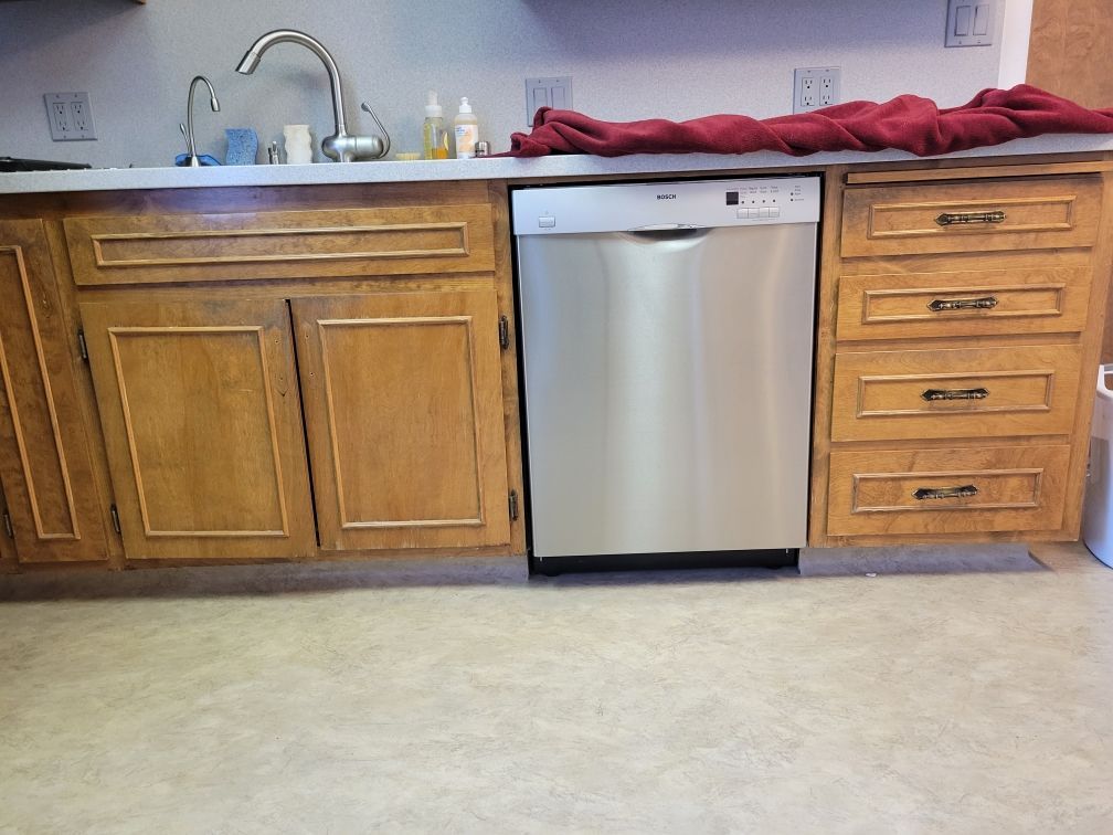Kitchen with wooden cabinets, stainless steel dishwasher, sink, and red cloth on the counter.