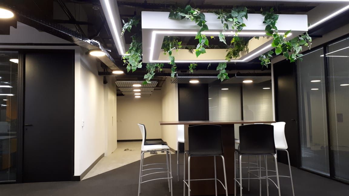 Sala de estar moderna com banquetas de bar, mesa alta, paredes de vidro e plantas suspensas.