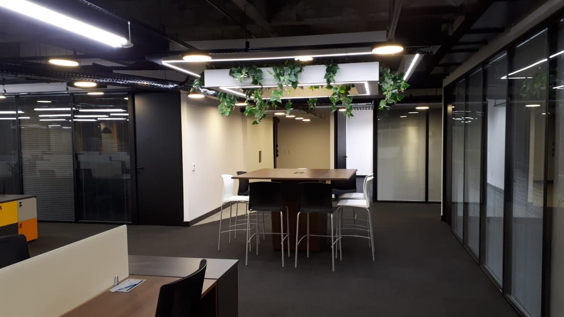 Sala de estar moderna com mesa central, banquetas, paredes de vidro e plantas suspensas.