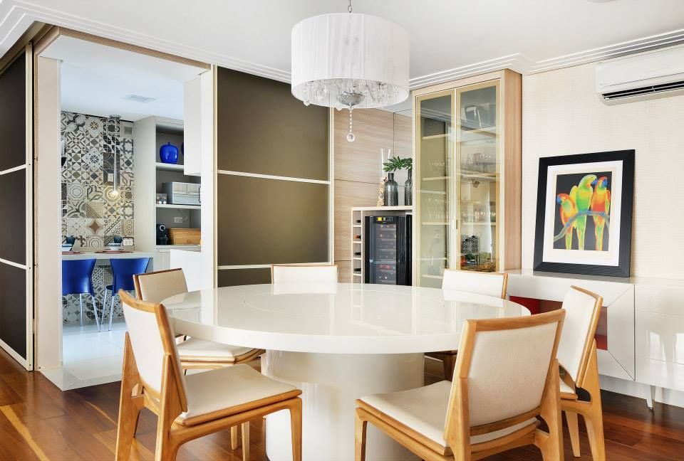 Sala de jantar moderna com mesa redonda branca, cadeiras de madeira, cristaleira e obras de arte coloridas na parede.