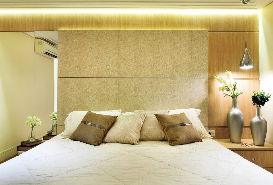 Quarto moderno com cama branca, cabeceira bege e iluminação aconchegante, decorado com plantas e vasos.