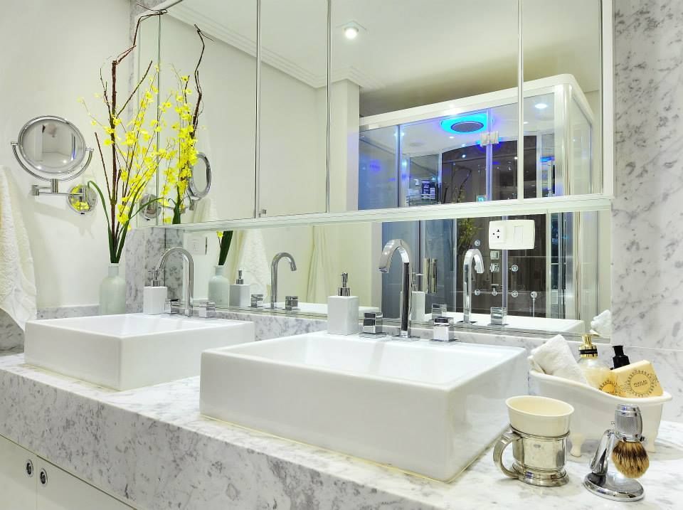 Móvel de banheiro branco brilhante com duas cubas, bancada de mármore e espelho refletindo a área do chuveiro.