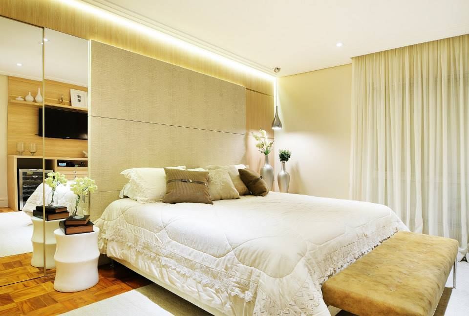 Quarto moderno e luminoso com uma grande cama branca, detalhes em bege, armário com espelho e cortinas translúcidas.